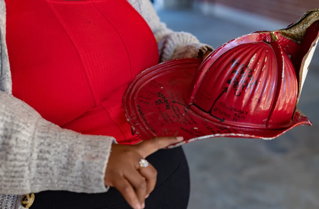 Diamond Jones' hand pointing to names on the red Comstock fire helmet